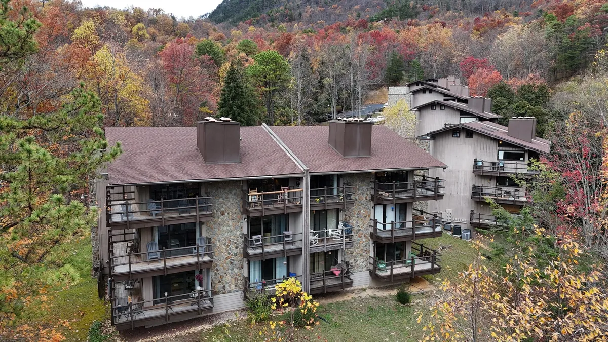 This image showcases the stone facade of a condo building framed by rich, colorful autumn foliage. Multiple balconies look out over the natural landscape, suggesting easy access to nature and inviting outdoor relaxation. The scene is serene and cozy, with hints of mountain exploration just beyond the property.