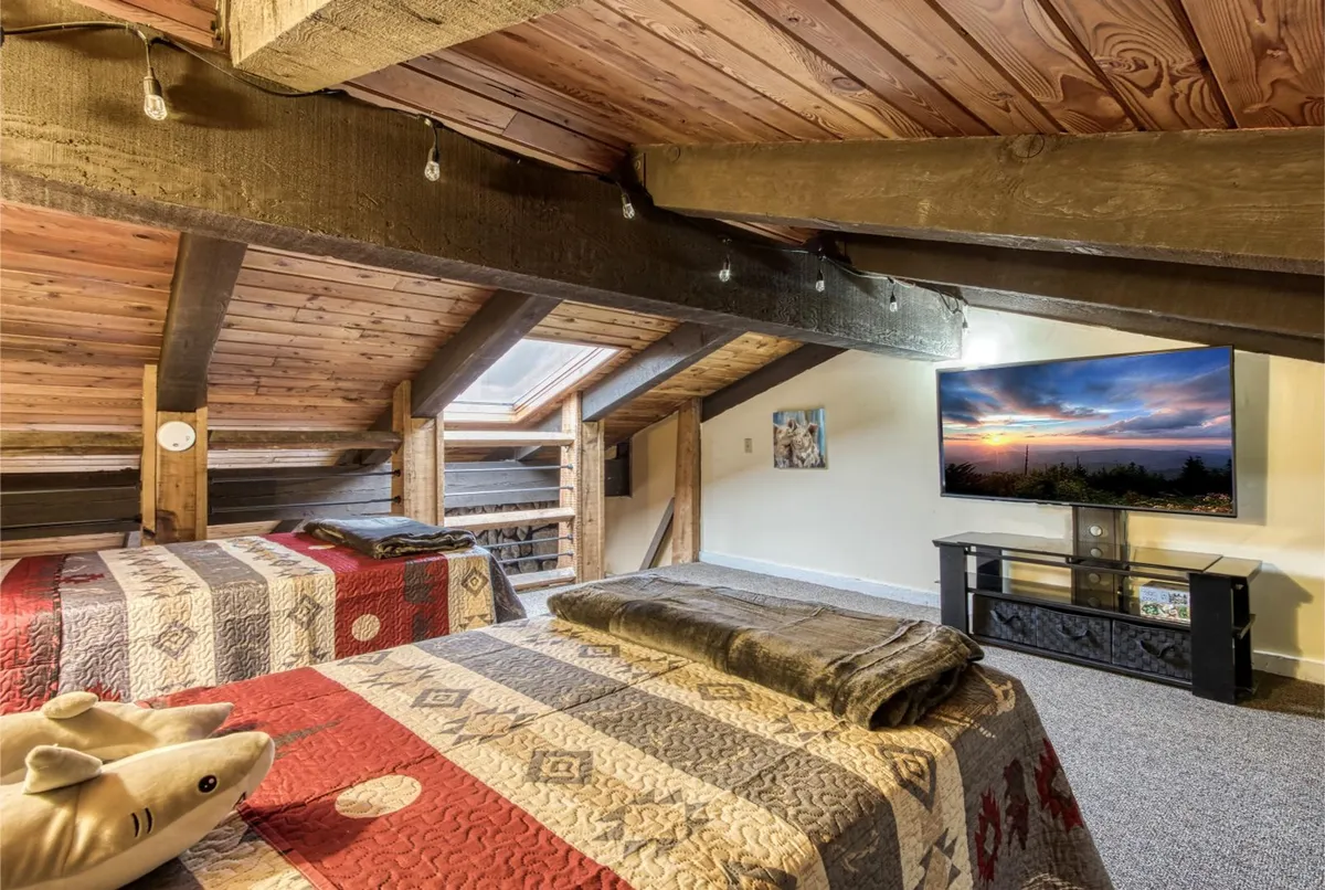 A welcoming bedroom scene featuring two beds with patterned quilts, a flat-screen TV, exposed wooden beams and ceiling, and decorative wall art. The soft lighting and cozy arrangement invite both couples and families to unwind after a day of adventure.