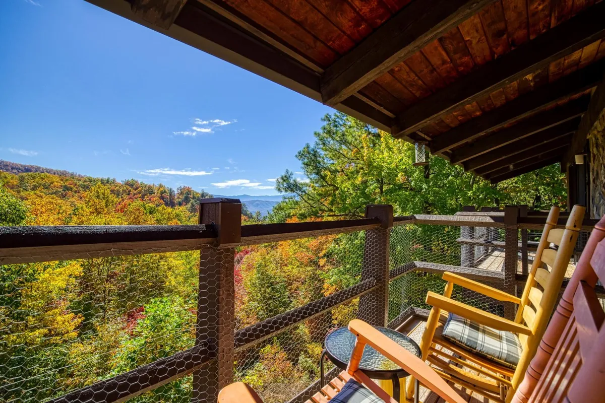 This image captures a private wooden deck furnished with classic rocking chairs, offering panoramic views of colorful autumn trees and a backdrop of Smoky Mountain landscapes. The calm, inviting atmosphere encourages relaxation and connection with nature.