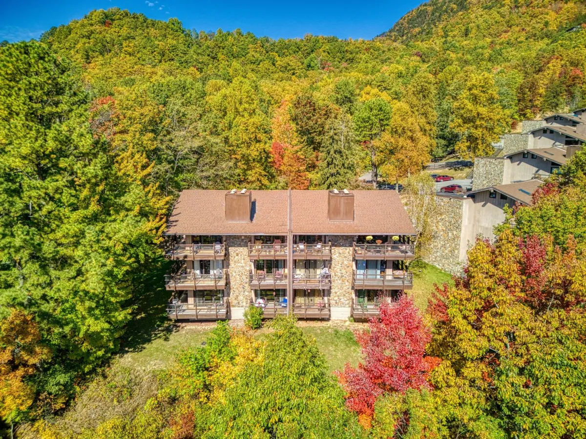The image showcases a multi-story stone condo nestled in a peaceful mountain setting, surrounded by vibrant autumn trees. Balconies with inviting outdoor furniture offer panoramic sunset views, and the overall scene radiates tranquility and seclusion.